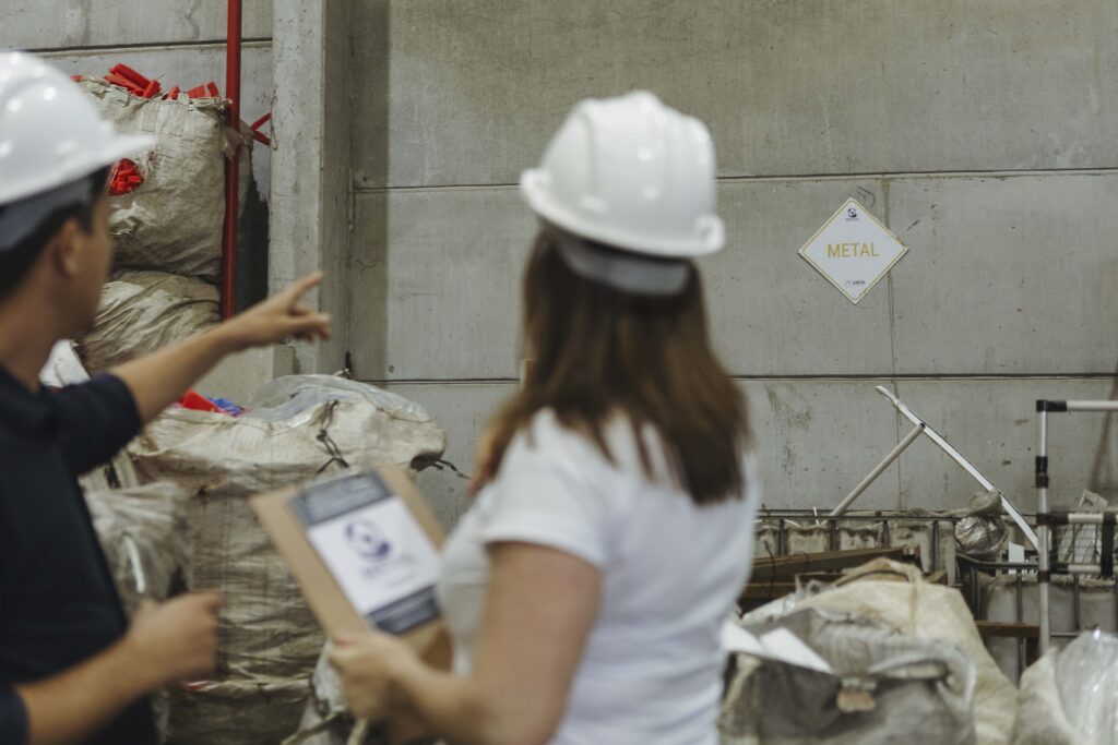 Profissionais com capacete analisando área de resíduos industriais, com identificação de material metálico em ambiente fabril